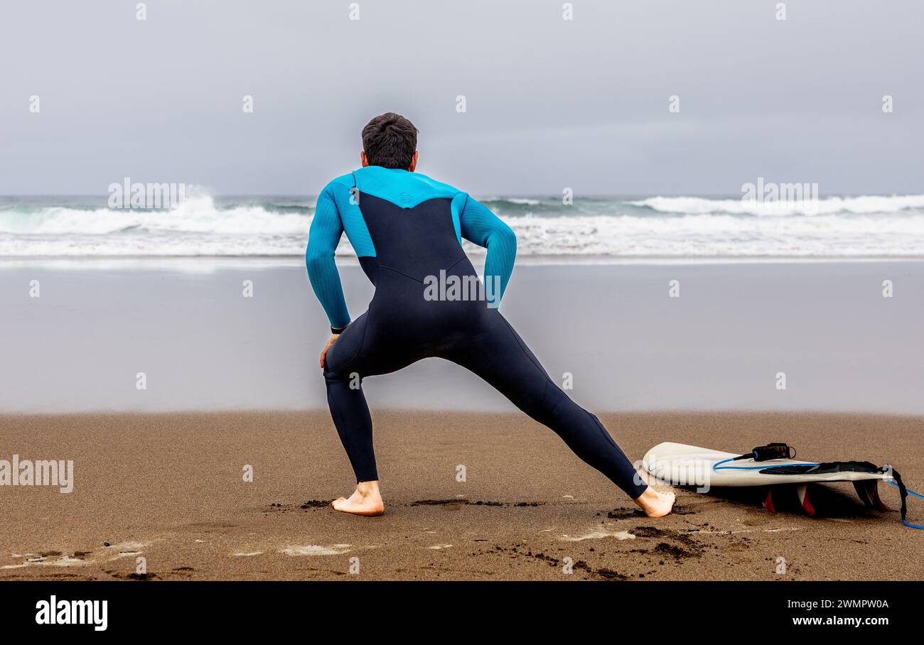 Young surfer warming up with flexibility exercises before entering the ...