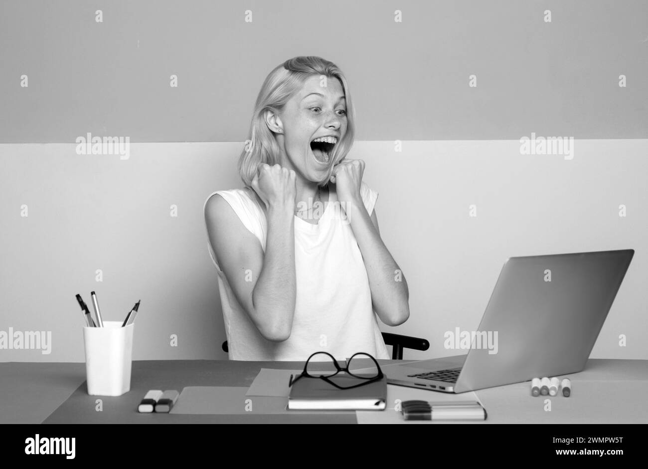 Female excited teacher use laptop at her desk marking students work. Pretty teacher smiling at camera at the school. University student. Stock Photo
