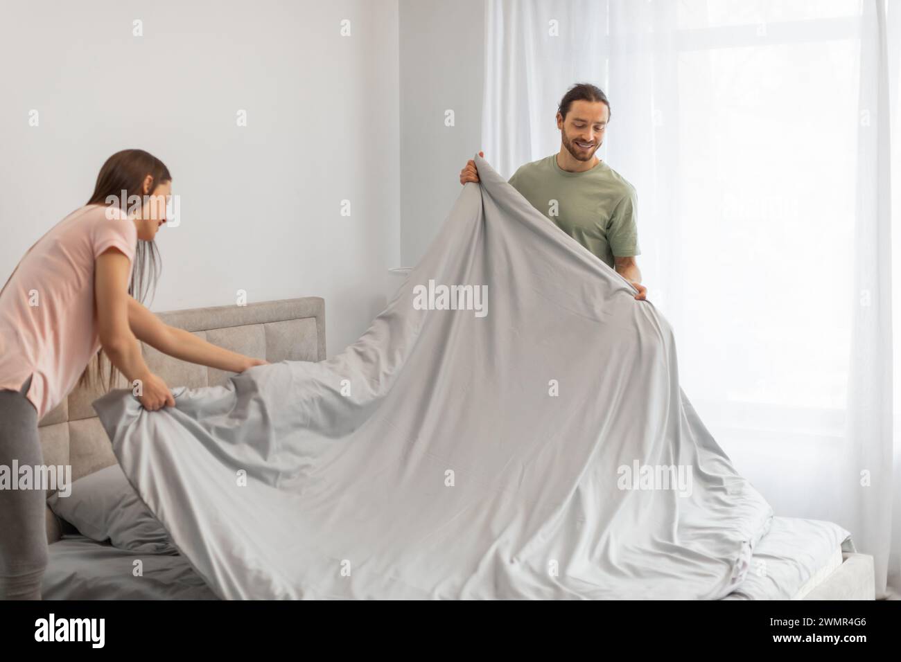 Happy couple making the bed together in morning Stock Photo