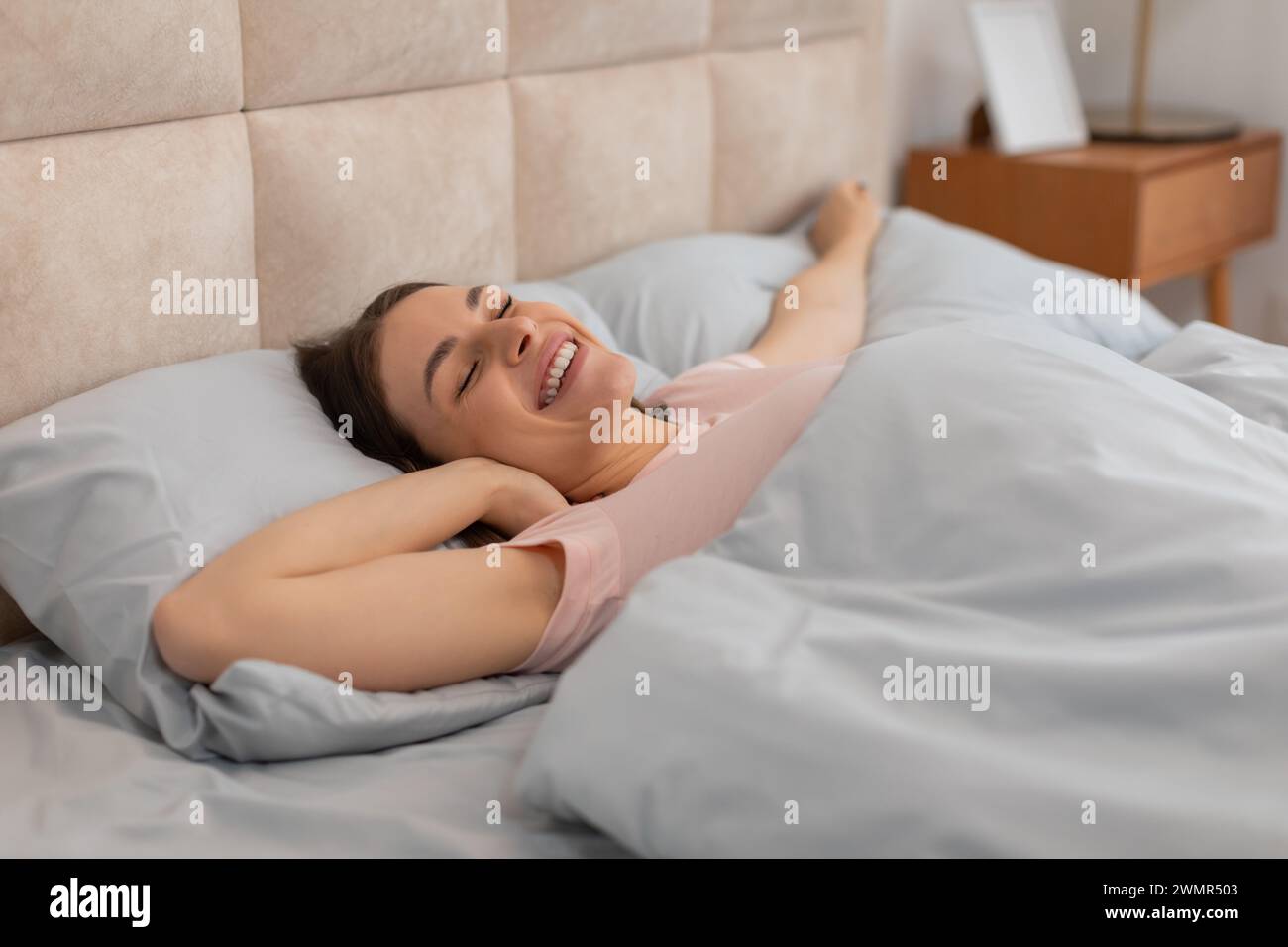 Woman stretching and smiling in bed, morning light Stock Photo