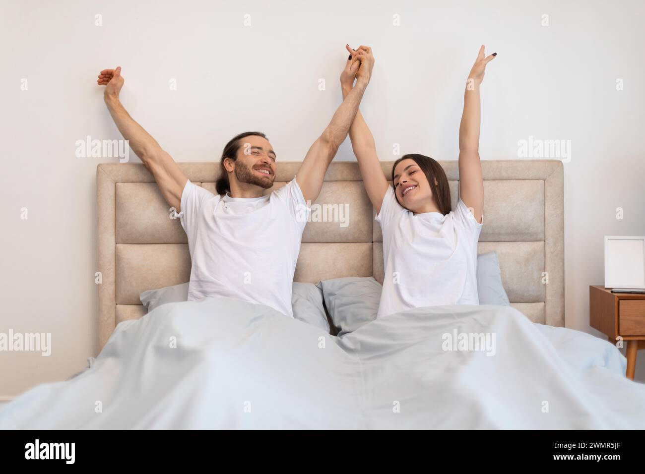 Couple stretching happily in bed after waking up Stock Photo