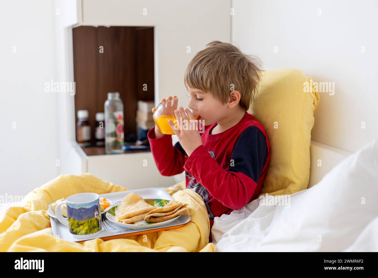 Sick child, toddler boy lying in bed with a fever, having breakfast white resting at home Stock Photo