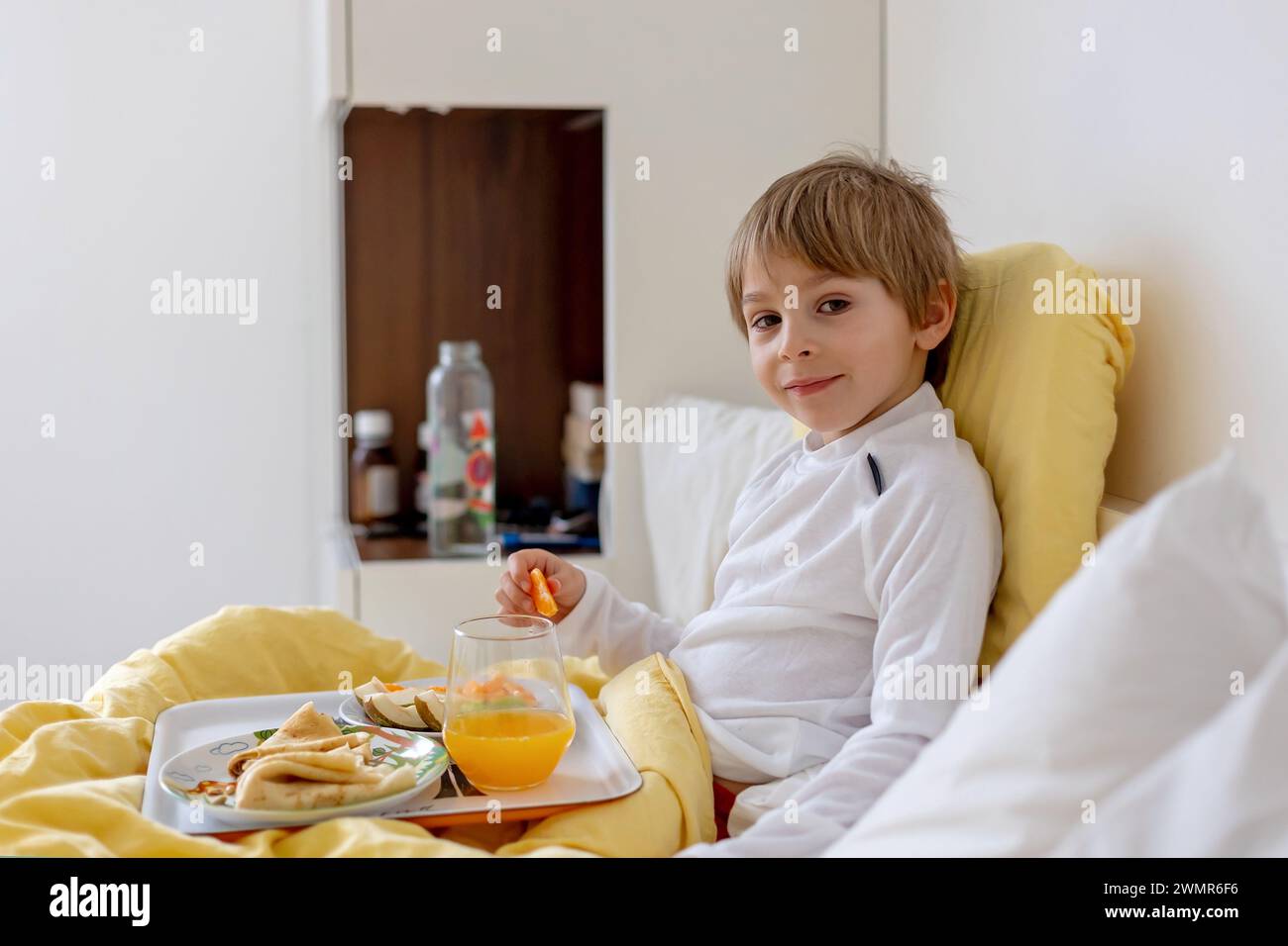 Sick child, toddler boy lying in bed with a fever, having breakfast white resting at home Stock Photo