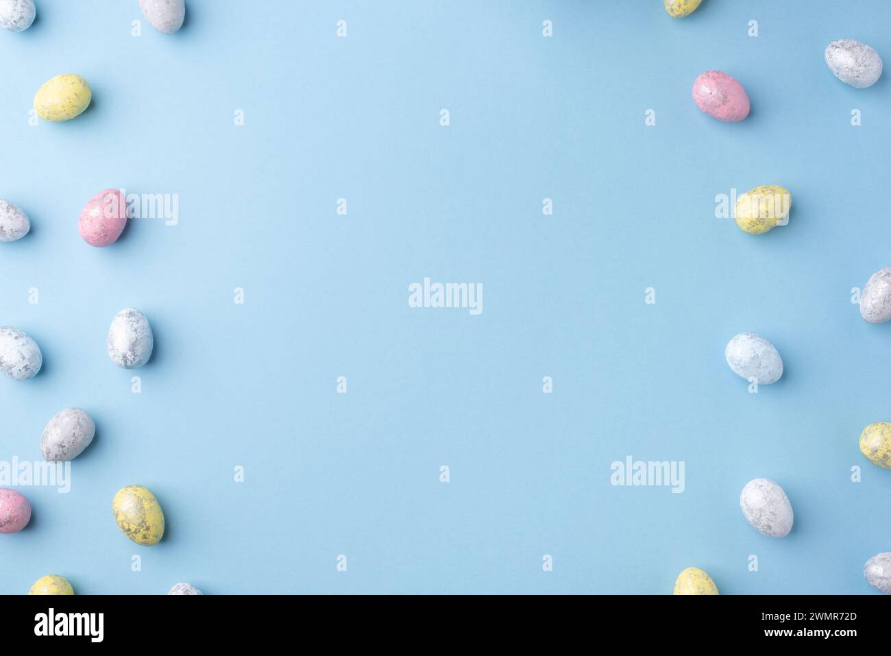 Festive Easter background. Multicoloured Easter eggs on a blue table. Card with a place for text. Top view. Stock Photo
