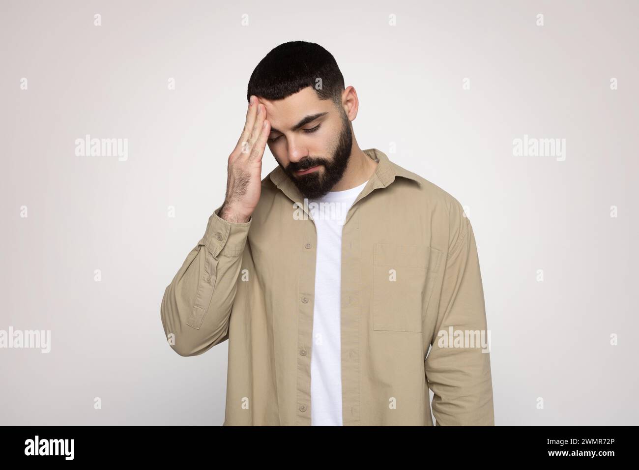 Man with a beard feeling stressed or having a headache, holding his forehead Stock Photo