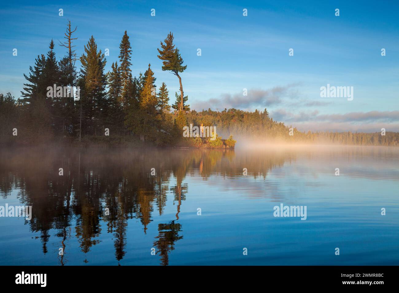 Blue trout lake and island in northern Minnesota with fog on the water at sunrise during September Stock Photo