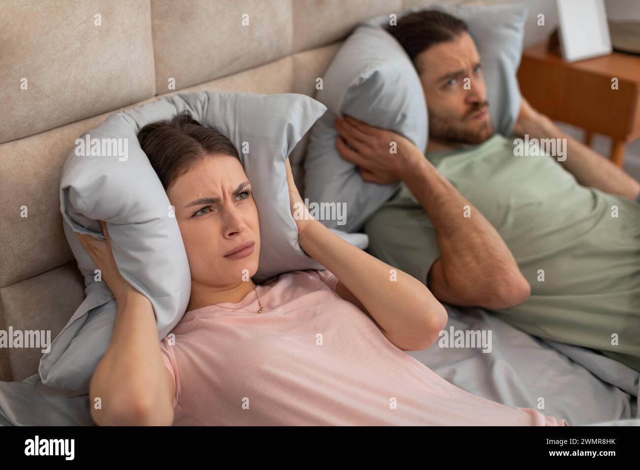 Disturbed couple covering ears with pillows in bed Stock Photo