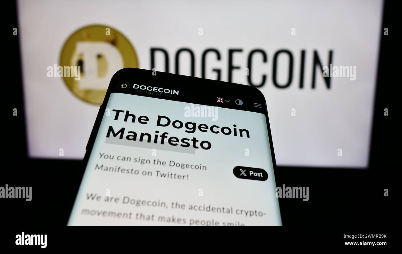 Mobile phone with website of cryptocurrency Dogecoin in front of logo. Focus on top-left of phone display. Stock Photo