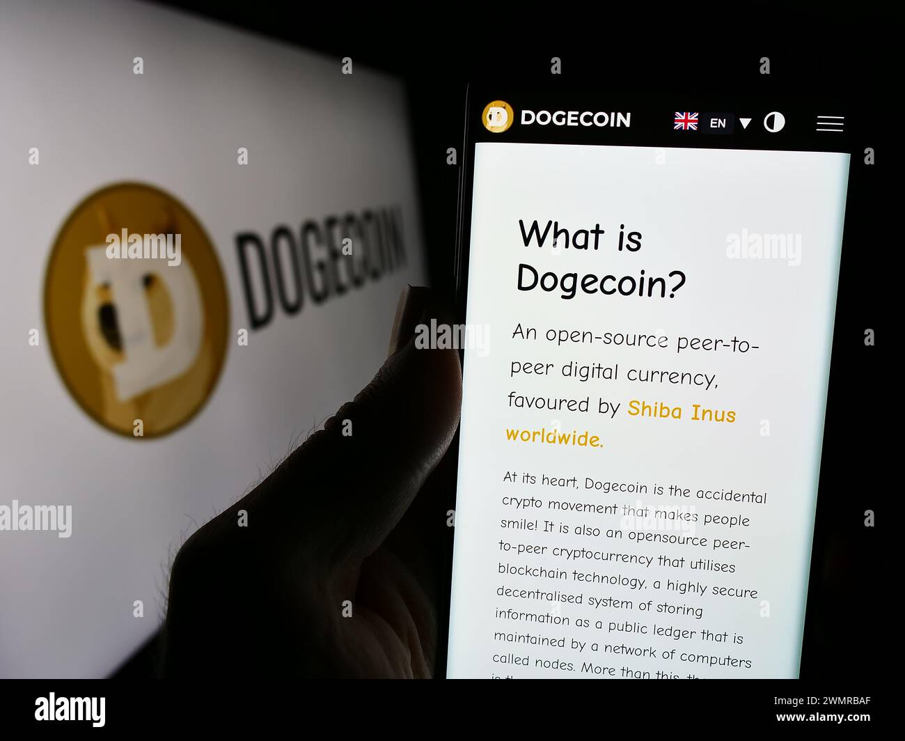 Person holding cellphone with webpage of cryptocurrency Dogecoin in front of logo. Focus on center of phone display. Stock Photo