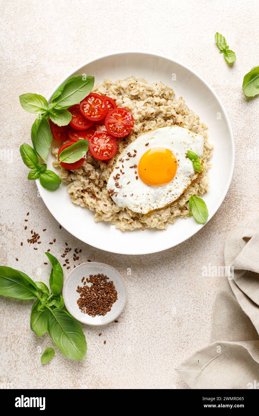 Oatmeal with fried sunny-side-up egg, tomatoes and basil, top view Stock Photo