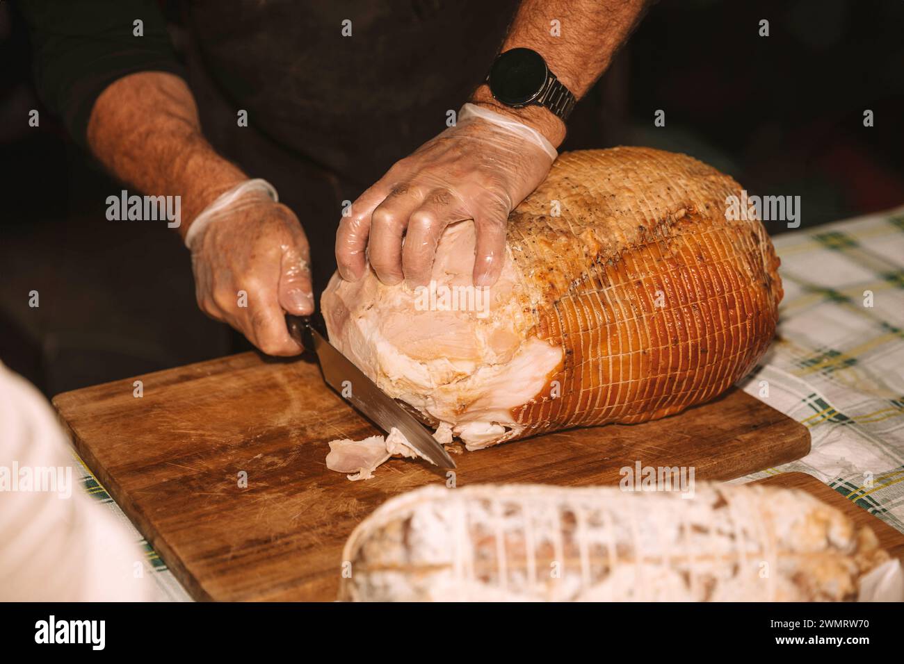 Chef's hands expertly slicing a large roasted ham Stock Photo