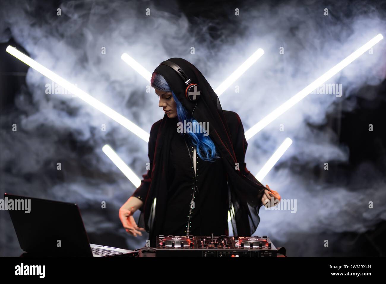 A female DJ with vibrant blue hair is actively mixing music at a ...