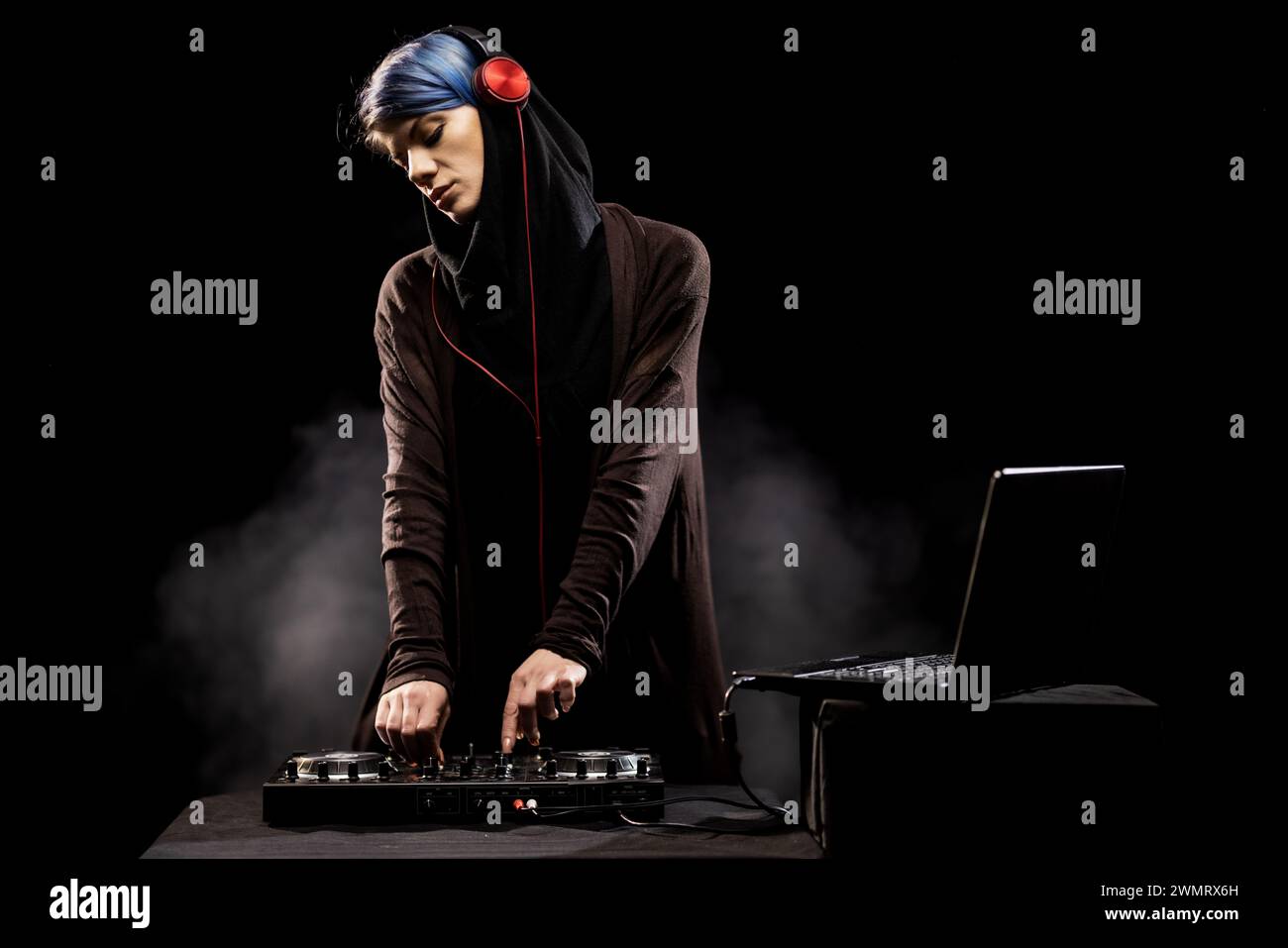 A woman wearing a hoodie is actively DJing music on a turntable. Smoke in the background Stock Photo