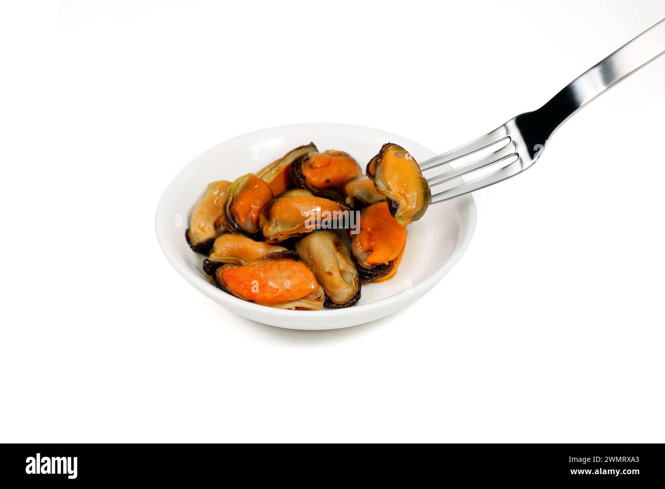 A fork picks up tinned canned smoked mussels from a dish, shellfish isolated on a white background. Stock Photo