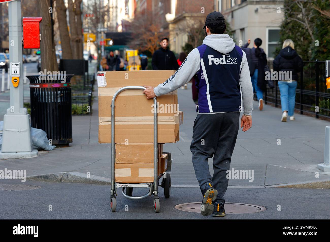 A FedEx worker with a hand truck full of packages walking across a street, New York, NYC. Stock Photo