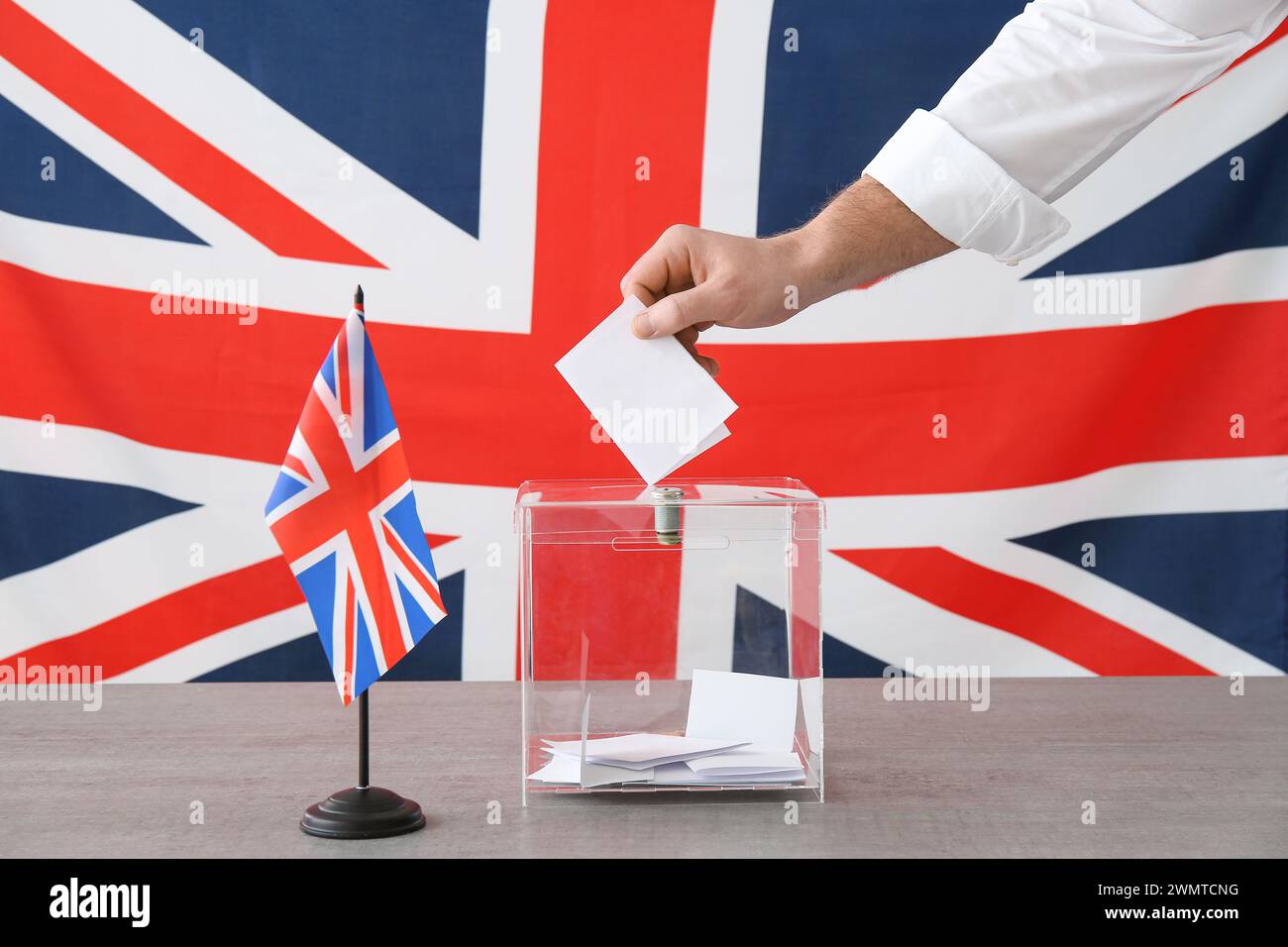 Voting young man with UK flag near ballot box on table at polling station, closeup Stock Photo