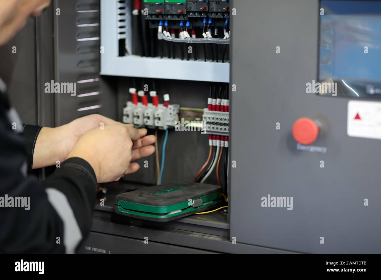 Electrician connecting wires in the control cabinet of industrial equipment. Industrial electrical panel. Selective focus. Stock Photo