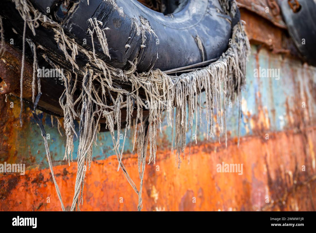 Old, damaged tyre fender with lines sticking out, on a steel hull of an