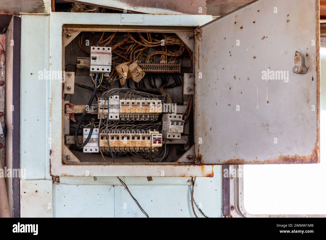 Old, rusty circuit breaker box with switches and cable wiring, inside view. Circuit breaker panel on damaged cargo ship bridge washed ashore, Stock Photo