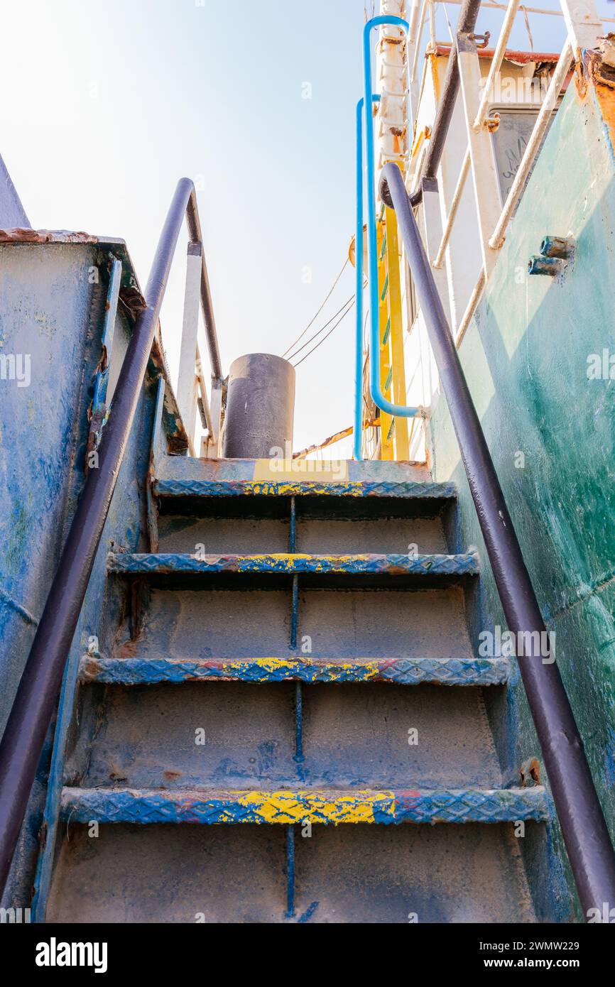 Old rusty vertical staircase with paint peeling off, leading to the upper deck of the wreck of cargo ship beached on the Al Hamriyah beach in UAE. Stock Photo