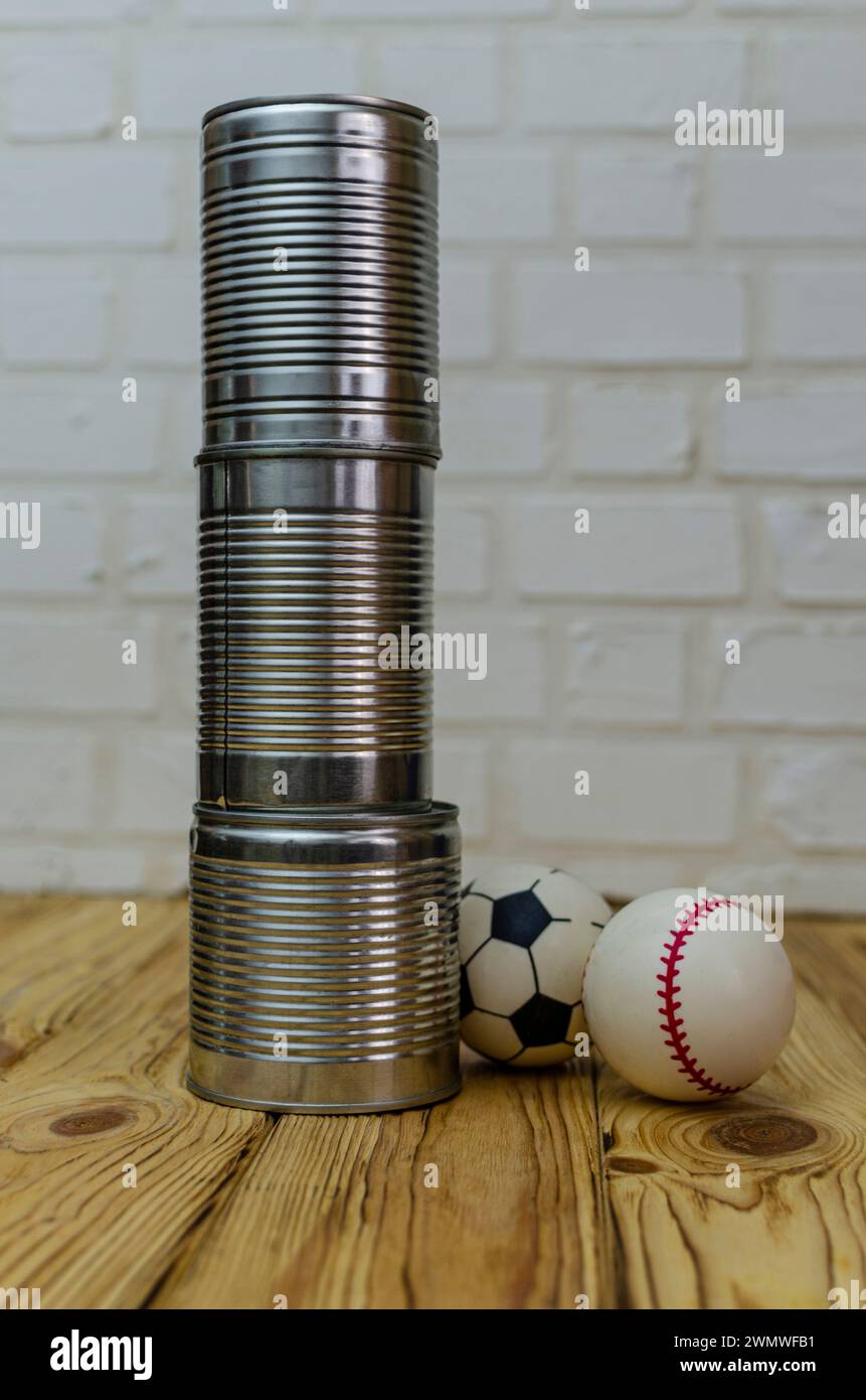 Three empty metal cans on a wooden surface against a white brick wall, two small balls, preparation for the game Stock Photo