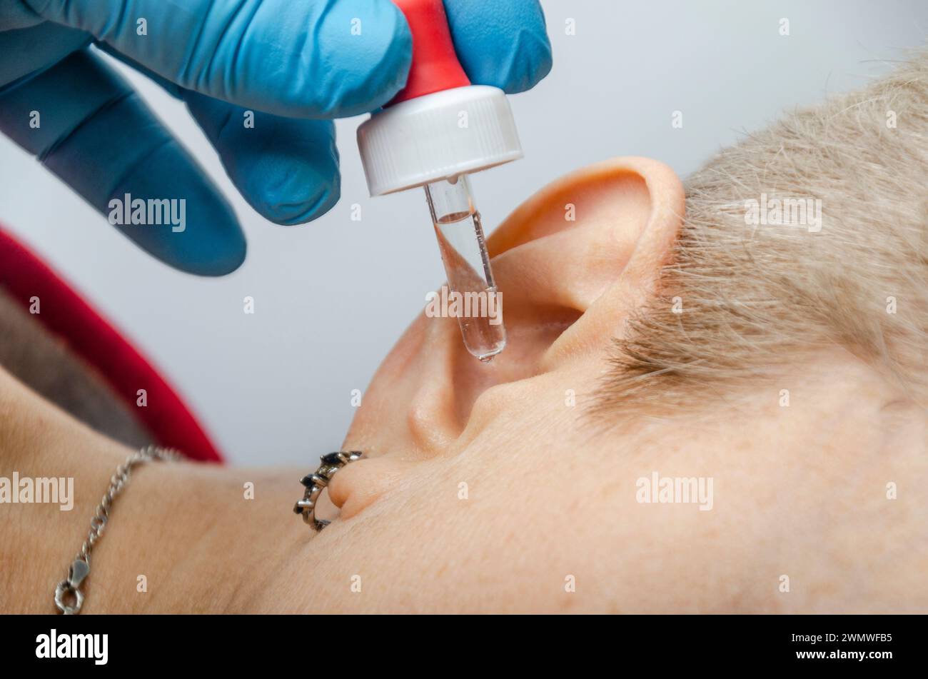 Medical pipette with a drop of medication over the patient's ear. Ear diseases Stock Photo