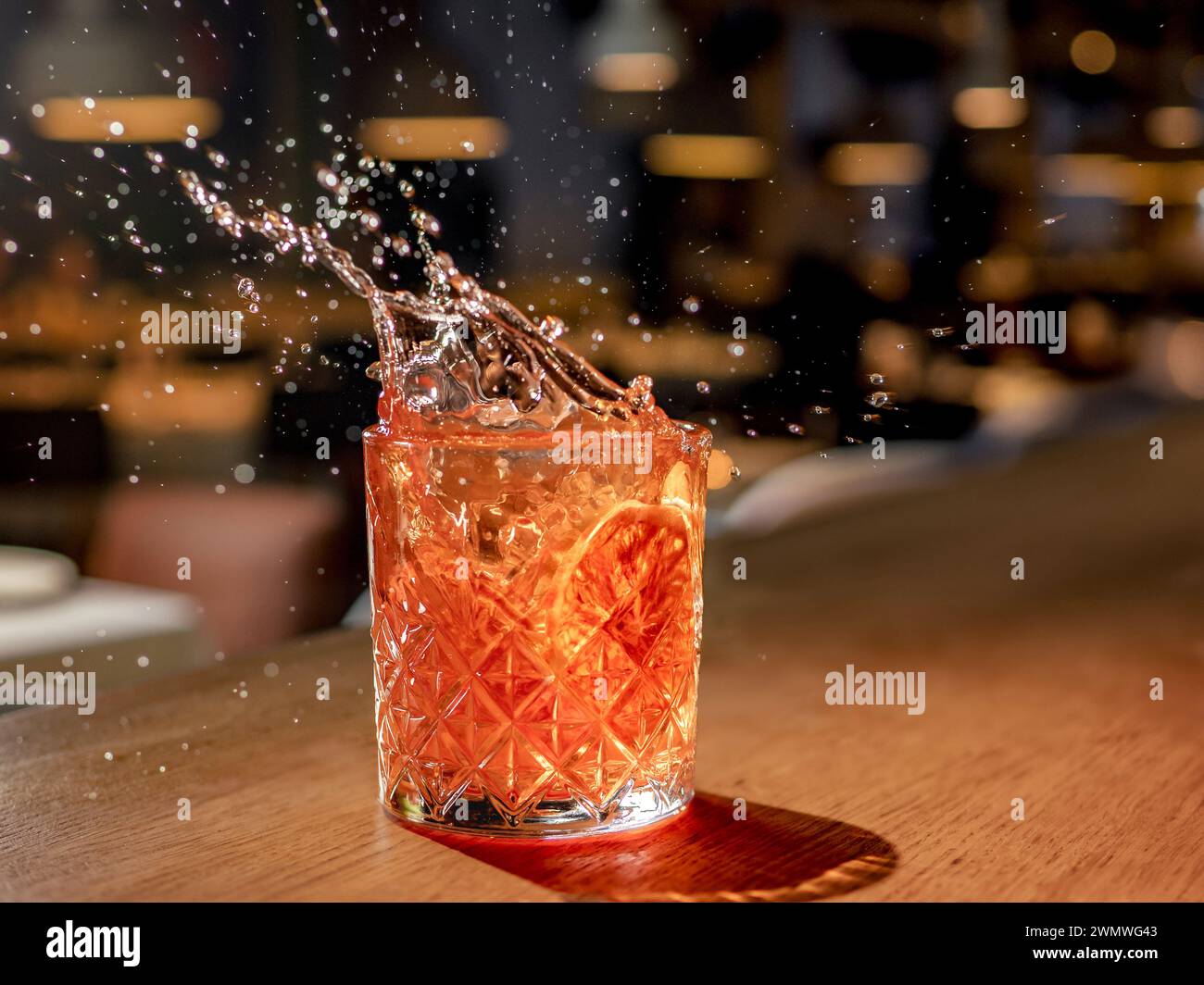 Orange or red drink with splash and droplets and orange slice garnish on bar counter. Red brown cocktail with splashes in pub or nightclub or restaurant Stock Photo