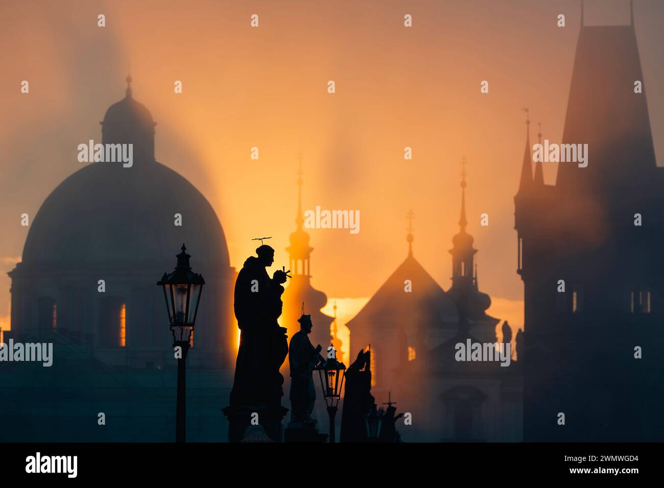 Statues on Charles Bridge against urban skyline with church and towers.  Beautiful sunrise in Prague, Czech Republic. Stock Photo