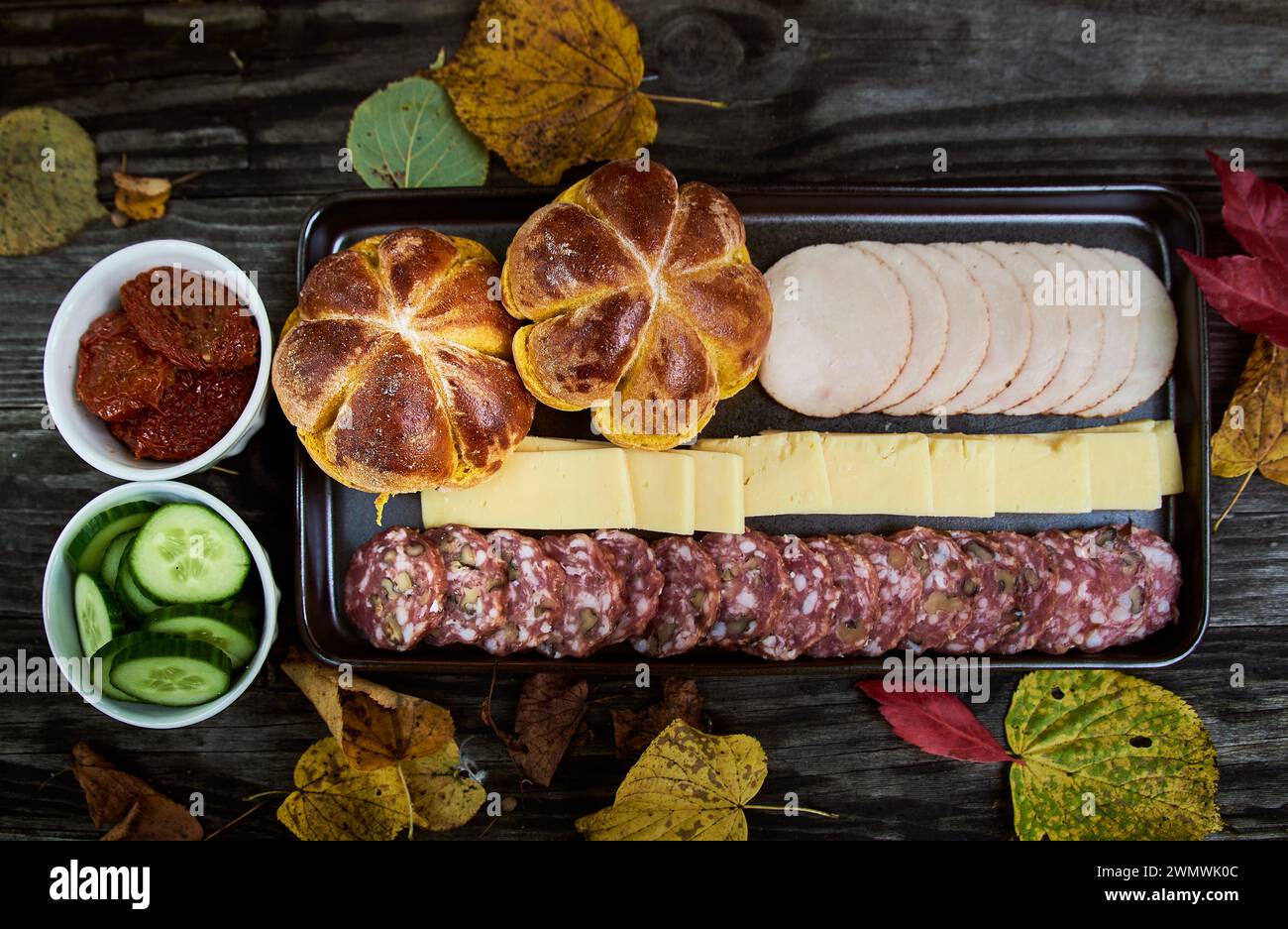 Top view autumnal picnic or outdoor meal with pumpkin panini, salami, ham and cheese on wooden background. Aerial view of food surrounded by leaves Stock Photo