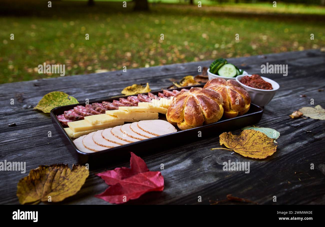 Autumnal picnic meal with panini shaped as pumpkin, cheese and salami. Food surrounded by fallen leaves in Autumn on a wooden bench. Delicious dish Stock Photo