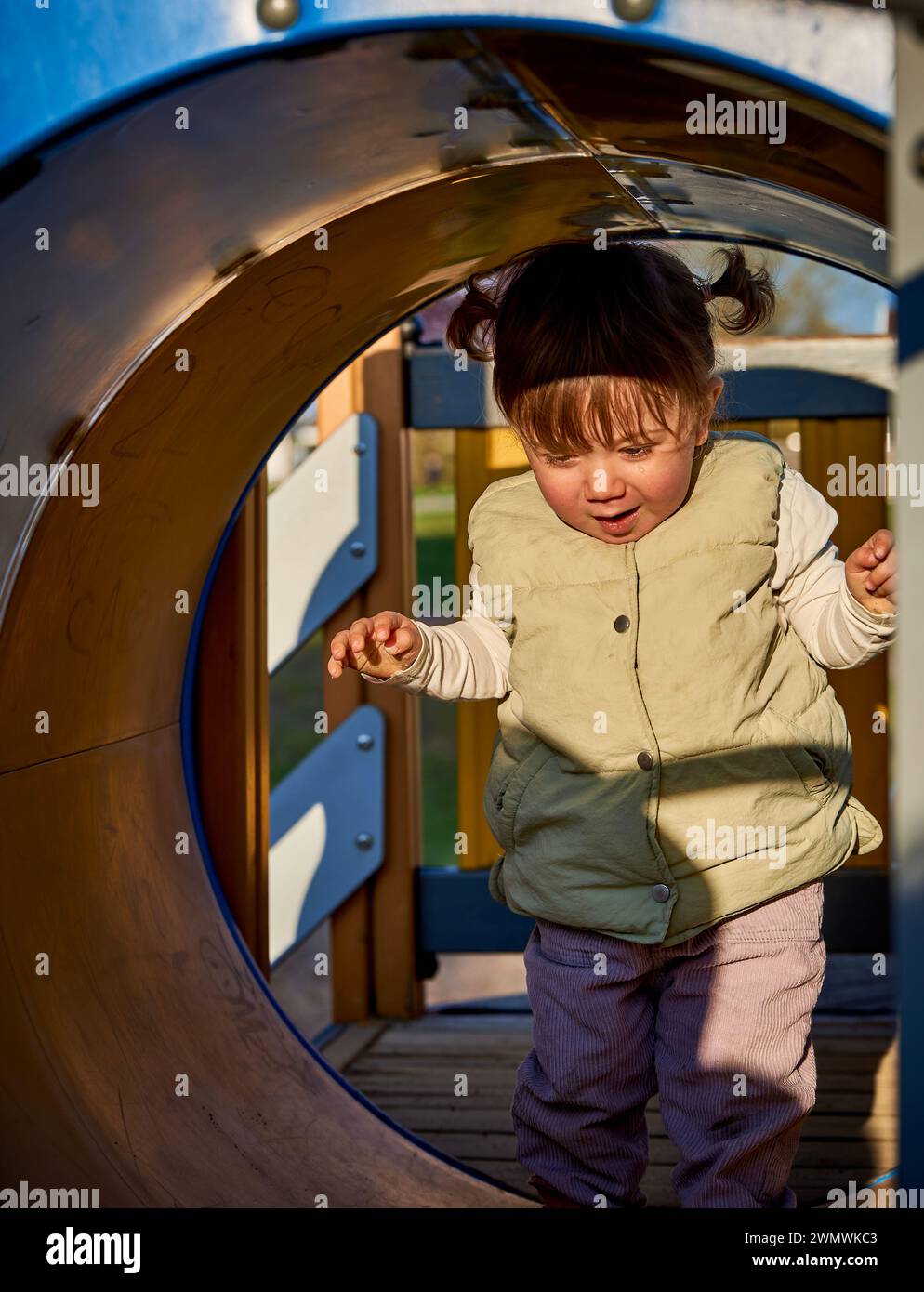 1 year old child learning to walk in a tunnel in the playground. Life discovery of a small female kid as she is walking thrilled and excited Stock Photo