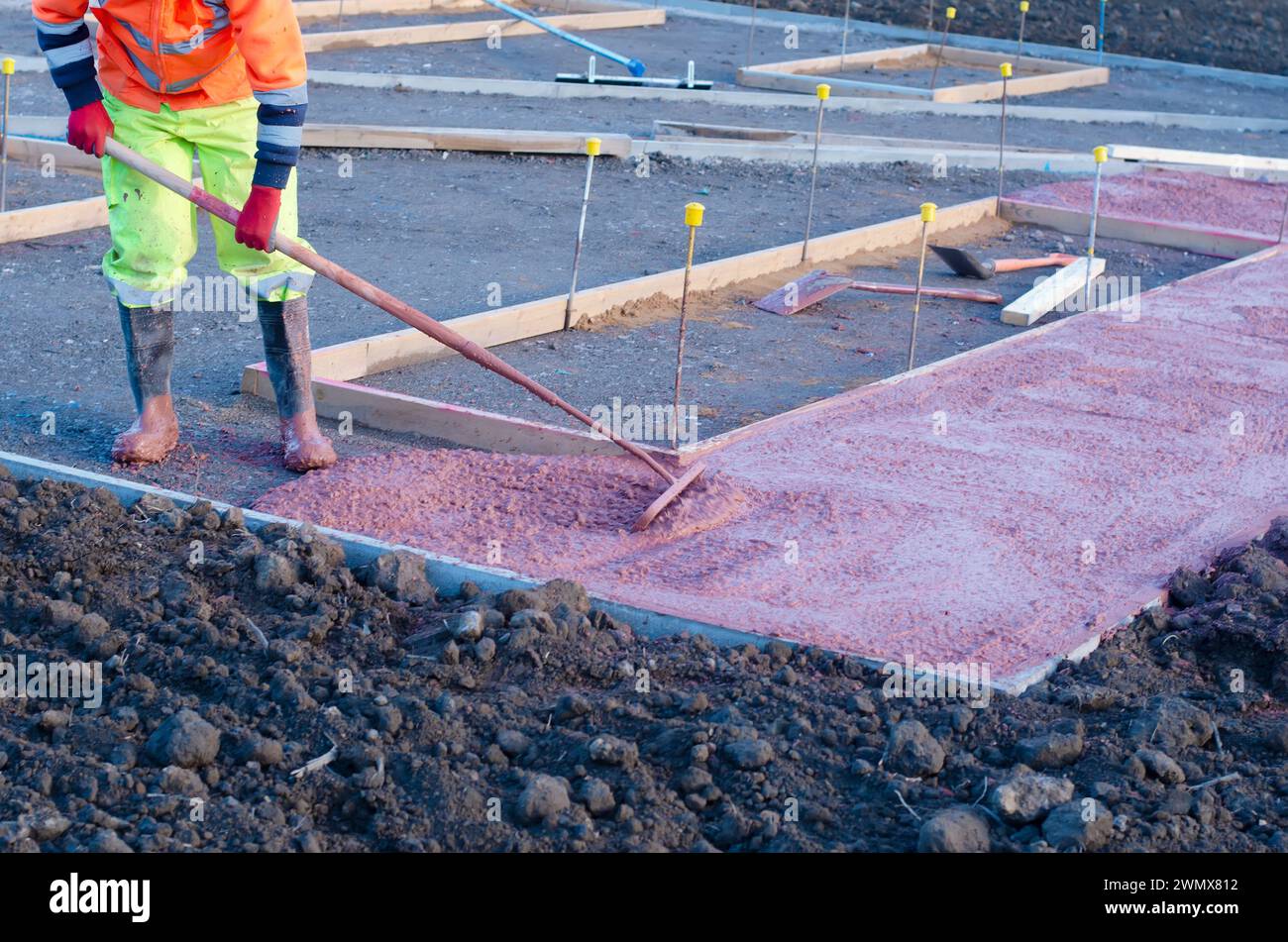 Builders pouring and leveling wet readymix concrete into formwork during new footpath