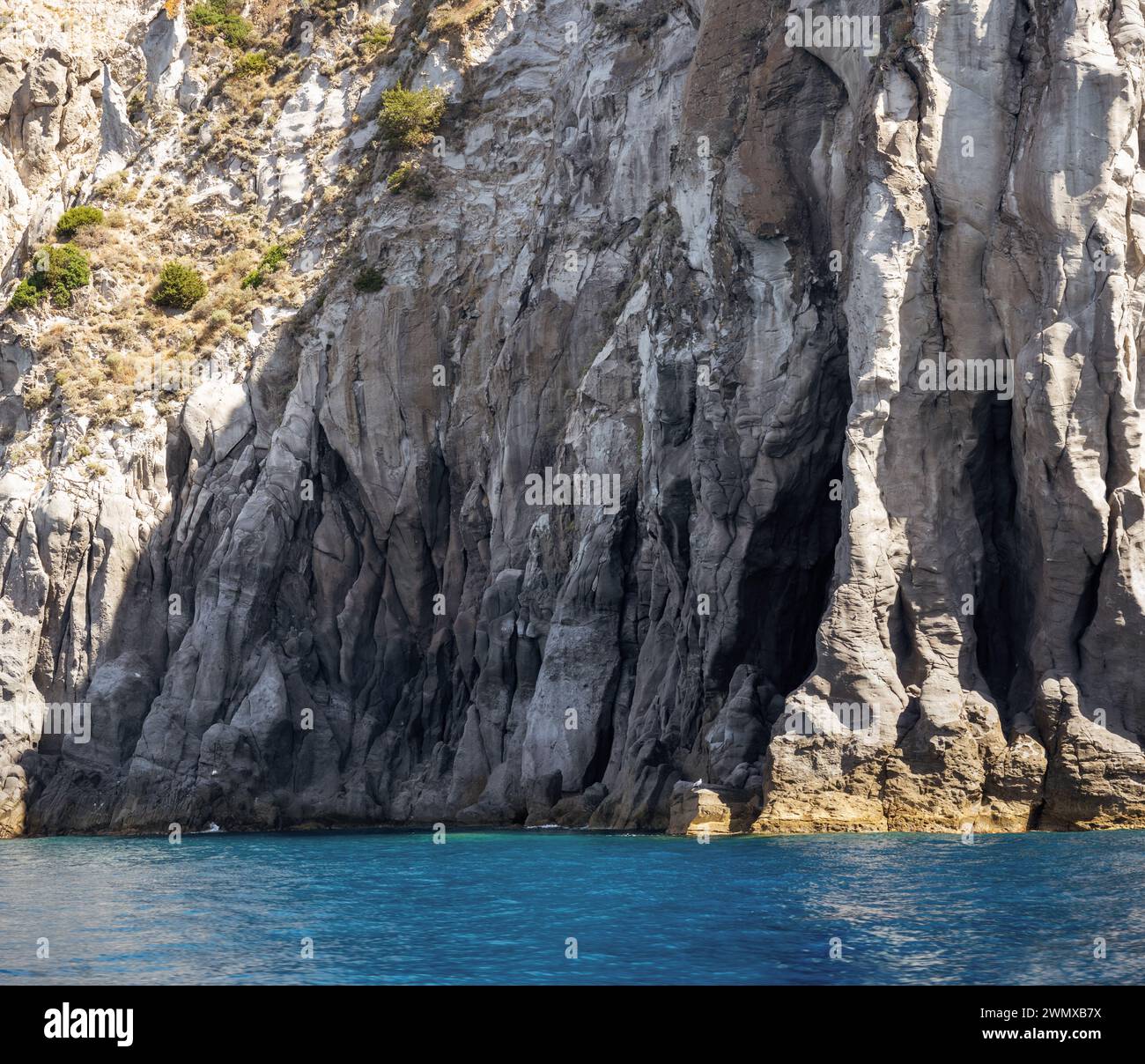 Weathered seaside rock face texture with parts of green and blue water ...