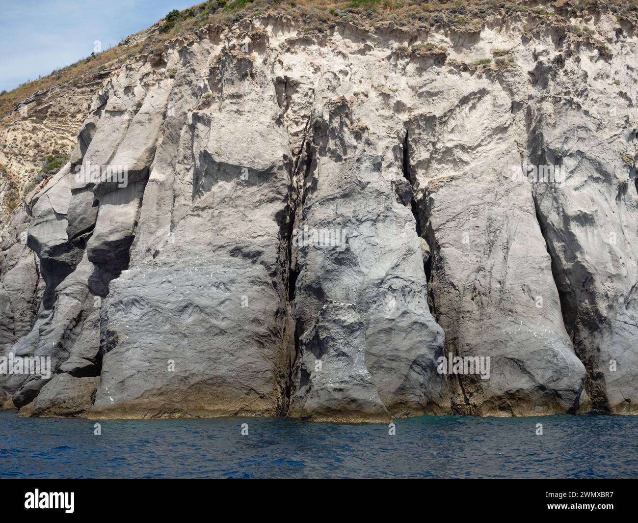 Weathered seaside rock face texture with parts of green and blue water ...