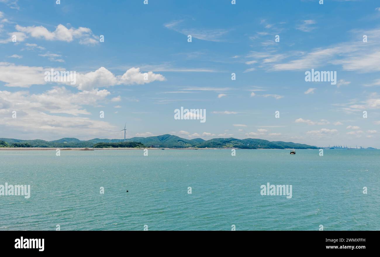 Seascape under blue cloudy sky with mountains and windmill in distance in South Korea Stock Photo
