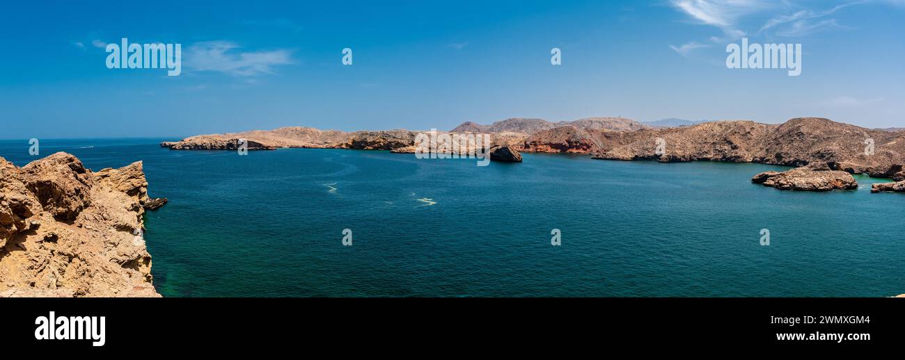 Panoramic views of a calm ocean with rocky coastline and clear blue skies, Oman Stock Photo