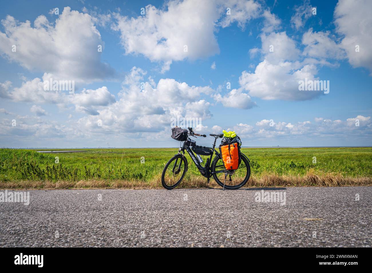 A loaded touring bike stands at the roadside with a wide field and open sky in the background, Westermarsch, Norden, East Frisia, Lower Saxony Stock Photo