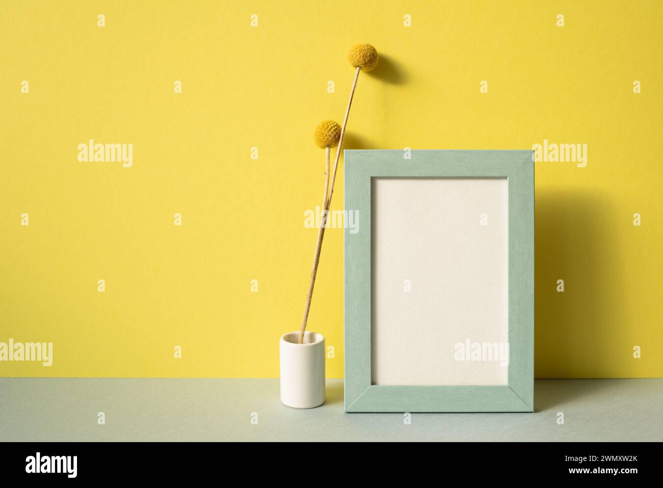 Photo frame with vase of dry flower on gray shelf. yellow wall background Stock Photo