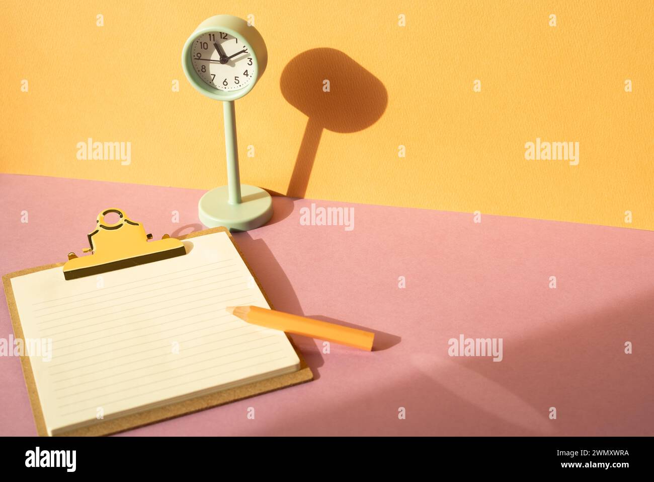 Clipboard and colored pencil, clock on pink desk. orange wall background. workspace Stock Photo