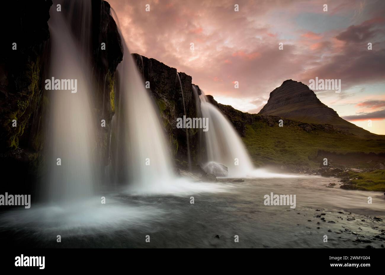 Smooth cascades of a majestic waterfall with the iconic Kirkjufell mountain at sunset in the background, captured in Iceland. Stock Photo