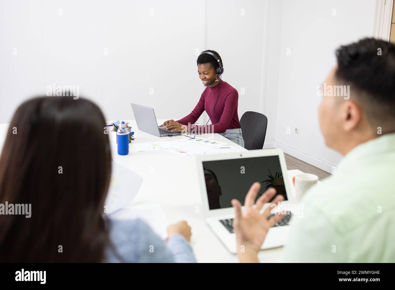 Young professionals engaged in a collaborative discussion in a bright office environment, using laptops and taking notes. Stock Photo
