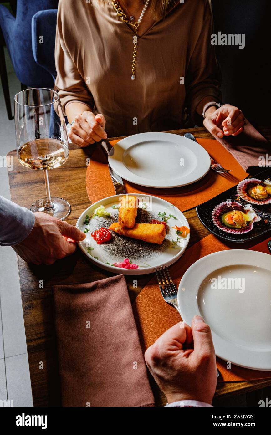 A refined dining setting featuring a woman at a table, a glass of wine and beautifully plated gourmet food, capturing the essence of fine dining Stock Photo