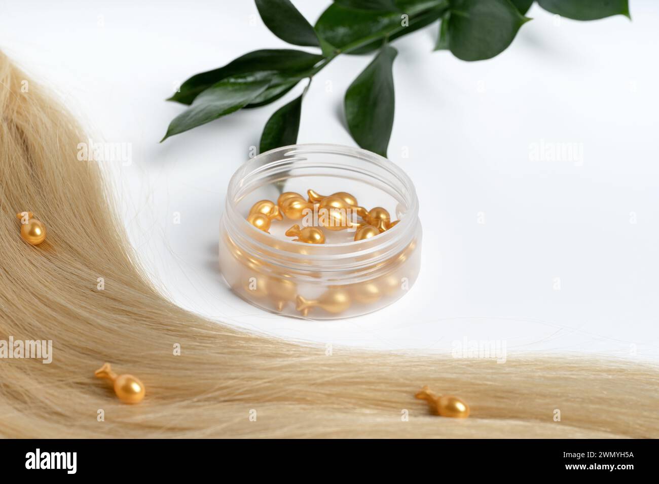 A close-up of golden serum capsules alongside a lock of blonde hair for nourishing hair care. Stock Photo