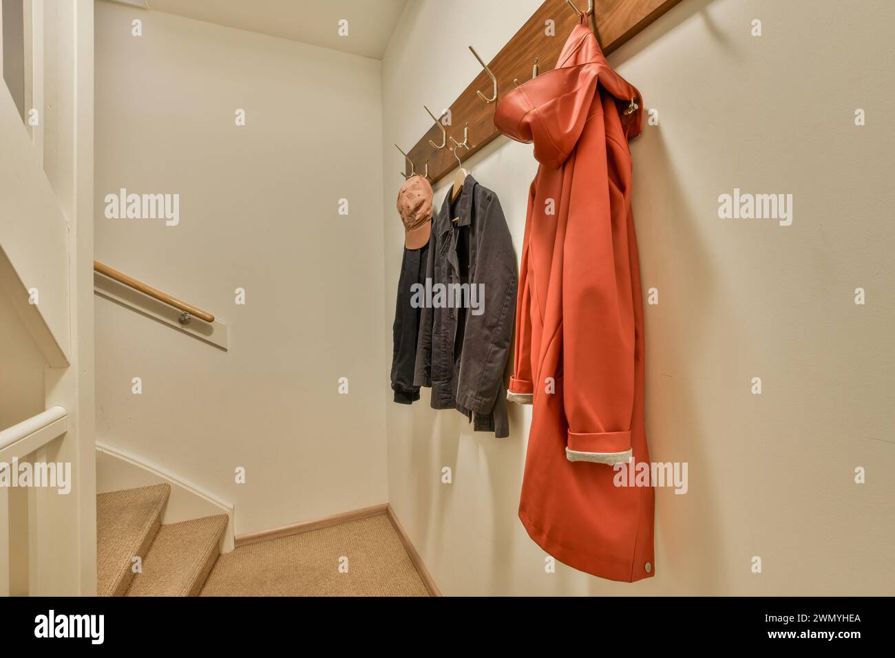 A warm and inviting home entryway features coats and hats neatly hung on wooden hooks, with a stair railing to the side. Stock Photo
