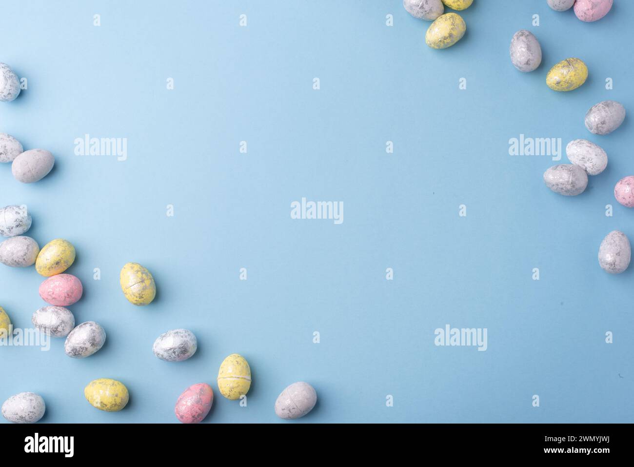 Festive Easter background. Multicoloured Easter eggs on a blue table. Card with a place for text. Top view. Stock Photo