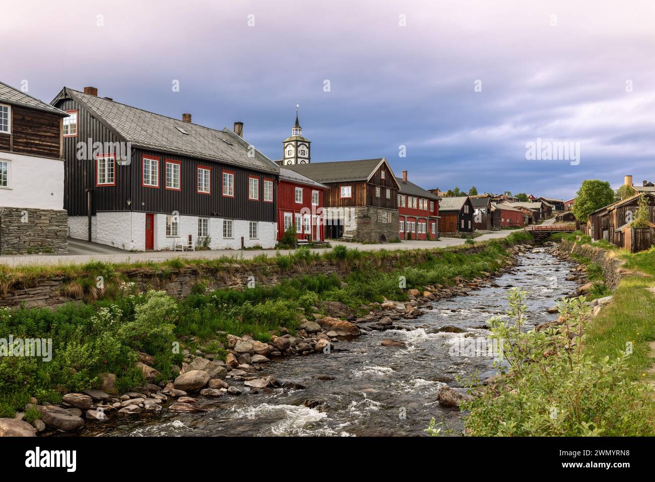 A serene view of the Glomma River flowing by historic wooden buildings in Roros, under a pastel-hued sky. Norway Stock Photo