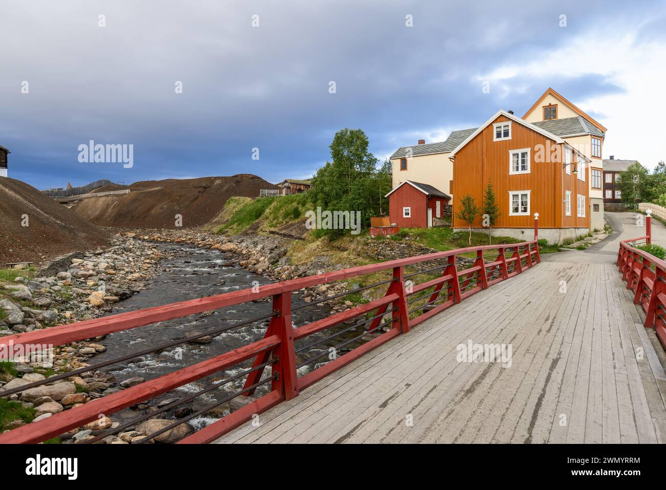 In Roros, a red bridge over the Glomma River provides a picturesque entrance to a street lined with traditional Norwegian wooden homes Stock Photo