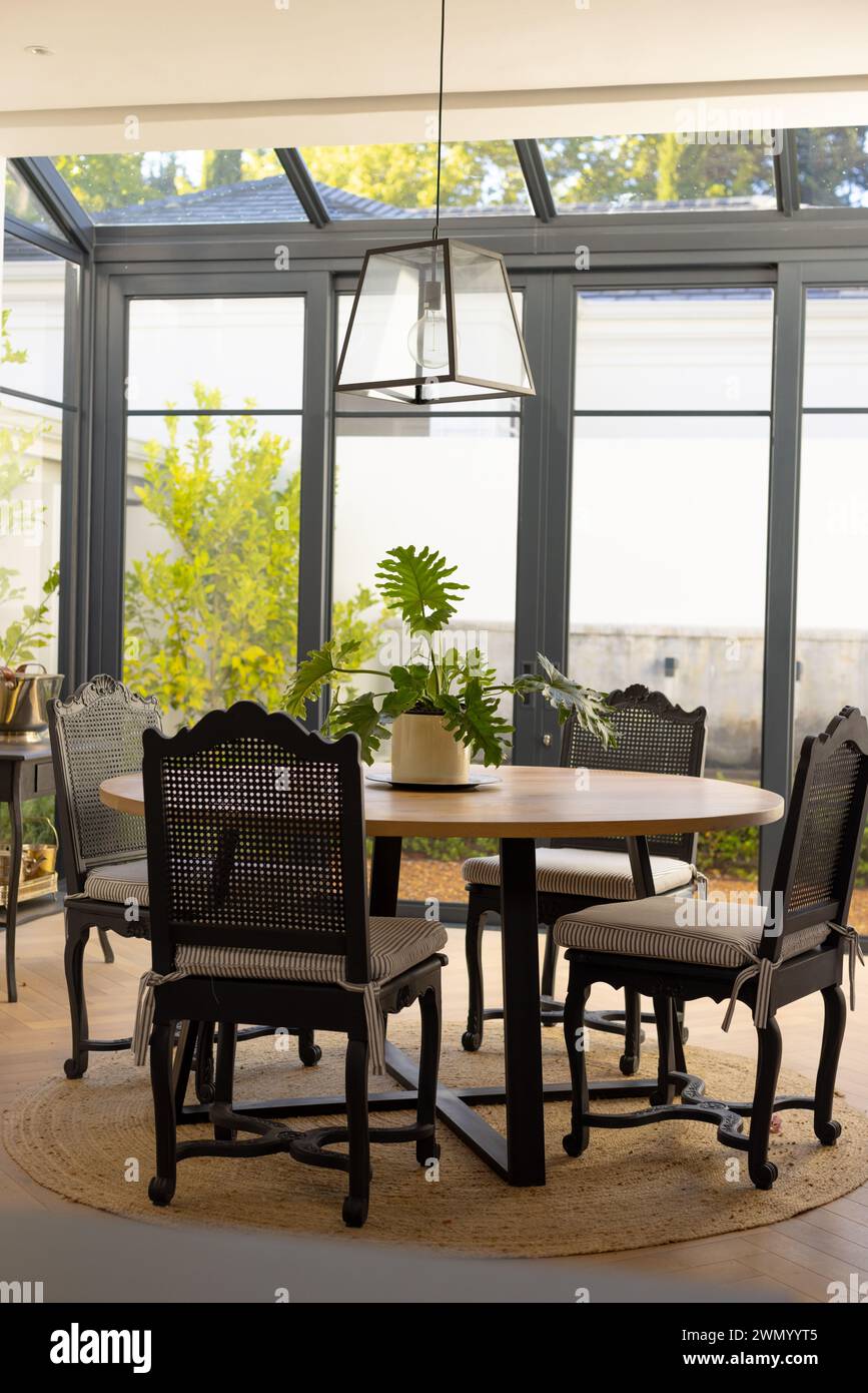 A well-lit dining area at home features a wooden table surrounded by black chairs Stock Photo