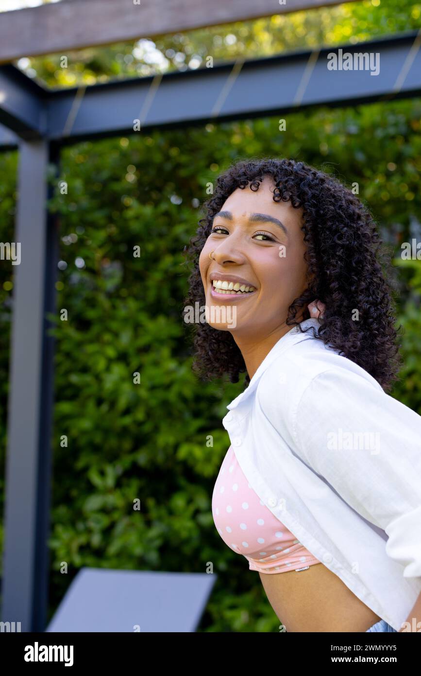 Young biracial woman with curly hair smiles brightly, wearing a pink ...