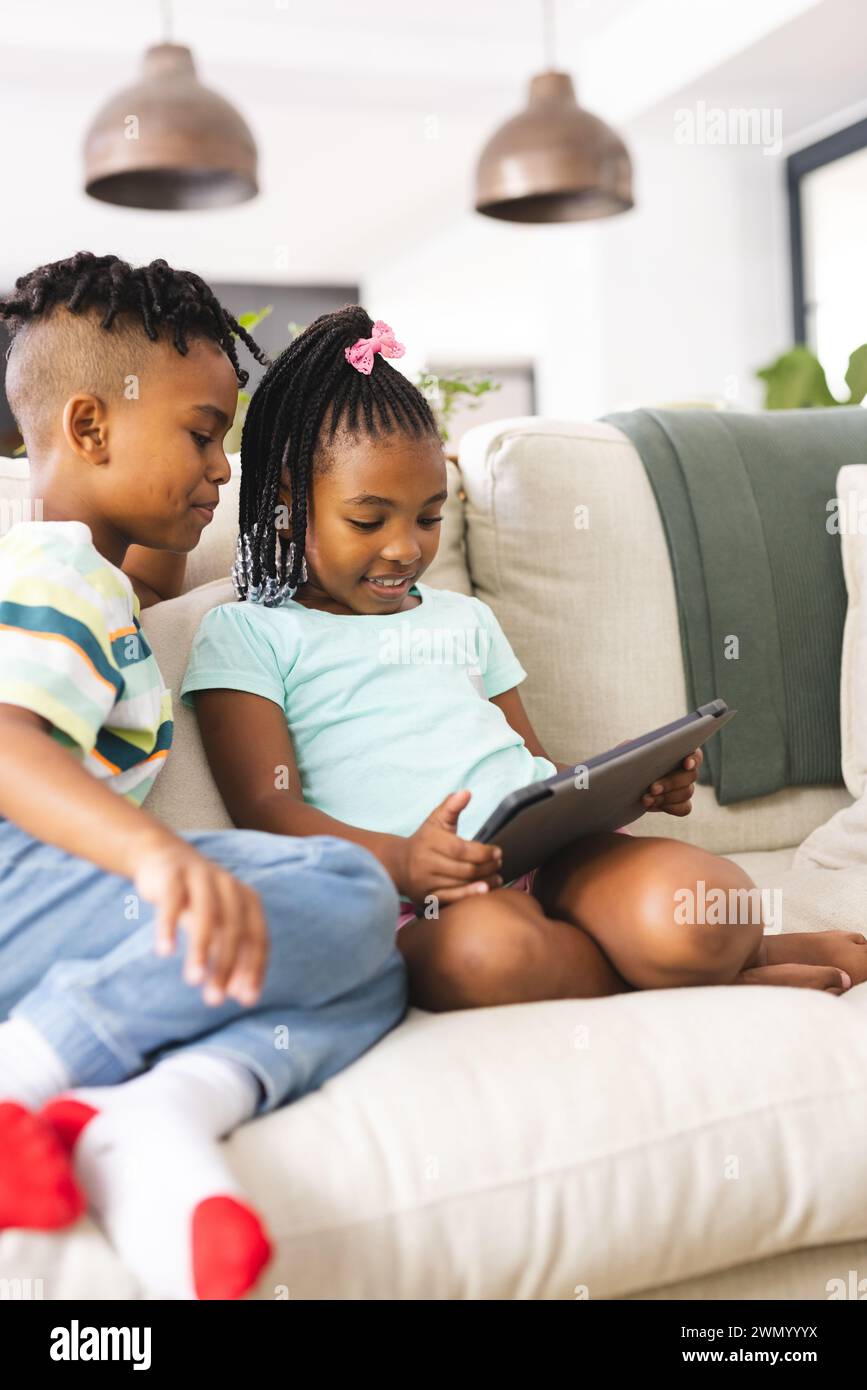 African American sister with pink hair accessory and brother using a tablet on a sofa Stock Photo